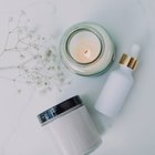 Une bougie, un flacon compte-gouttes et un pot de crème posés à plat sur un fond clair