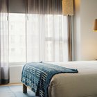 Une chambre d'hôtel, un plaid bleu posé au pied du lit devant une grande fenêtre