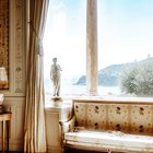Un salon ancien aux moulures dorées, une statue devant la fenêtre ouverte sur la mer